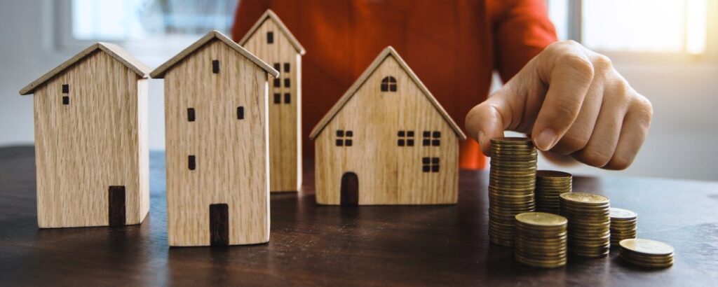 How much house can I afford shown with wooden model houses and stacks of coins